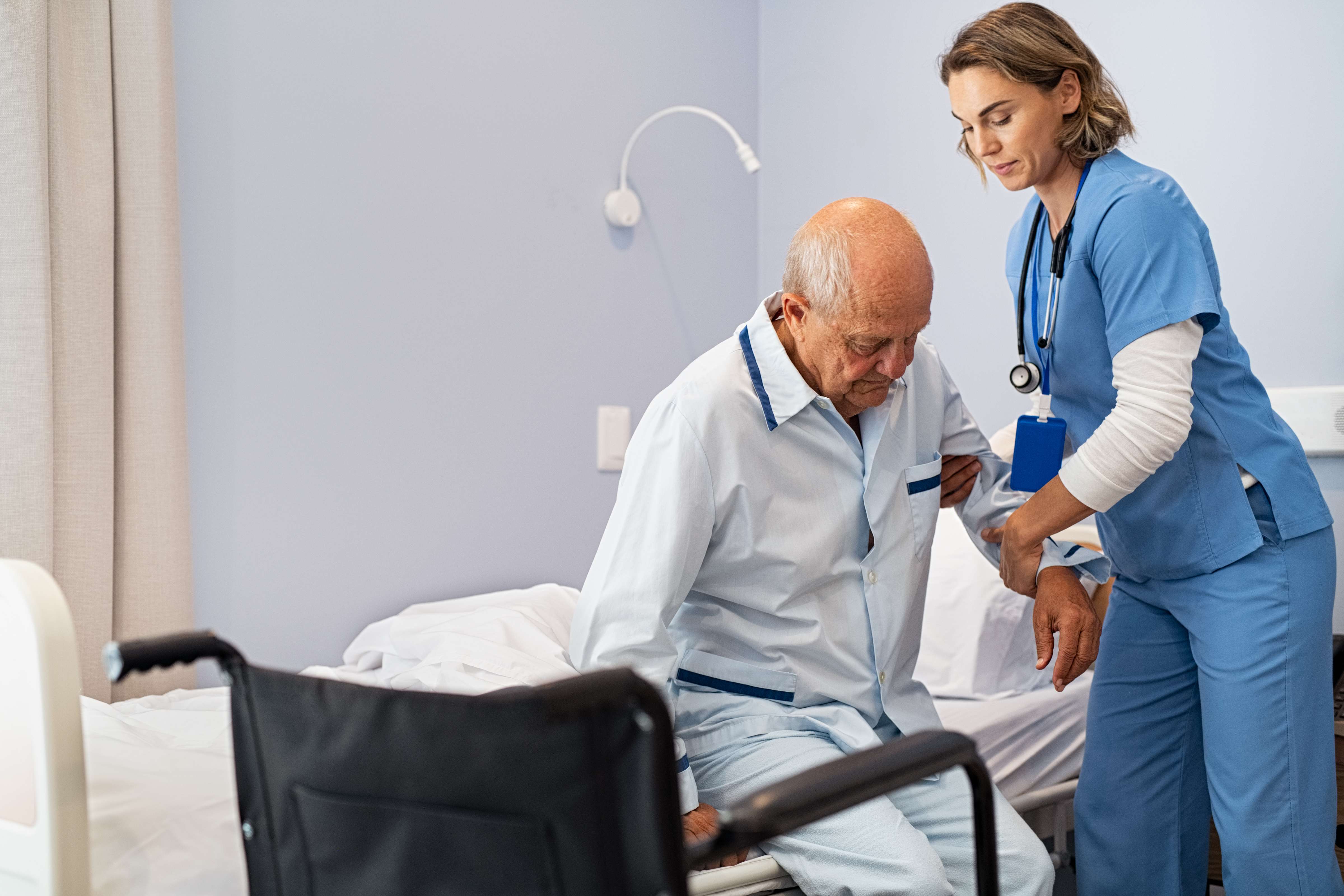A nurse assisting an older man to get up from bed in hospital