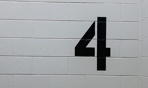 A photo of a black stencilled number 4 on a white brick wall. Photo by Kelly Sikkema on Unsplash.