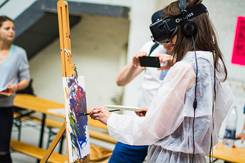 Woman painting while wearing virtual reality headset. Photo by Billetto Editorial on Unsplash.
