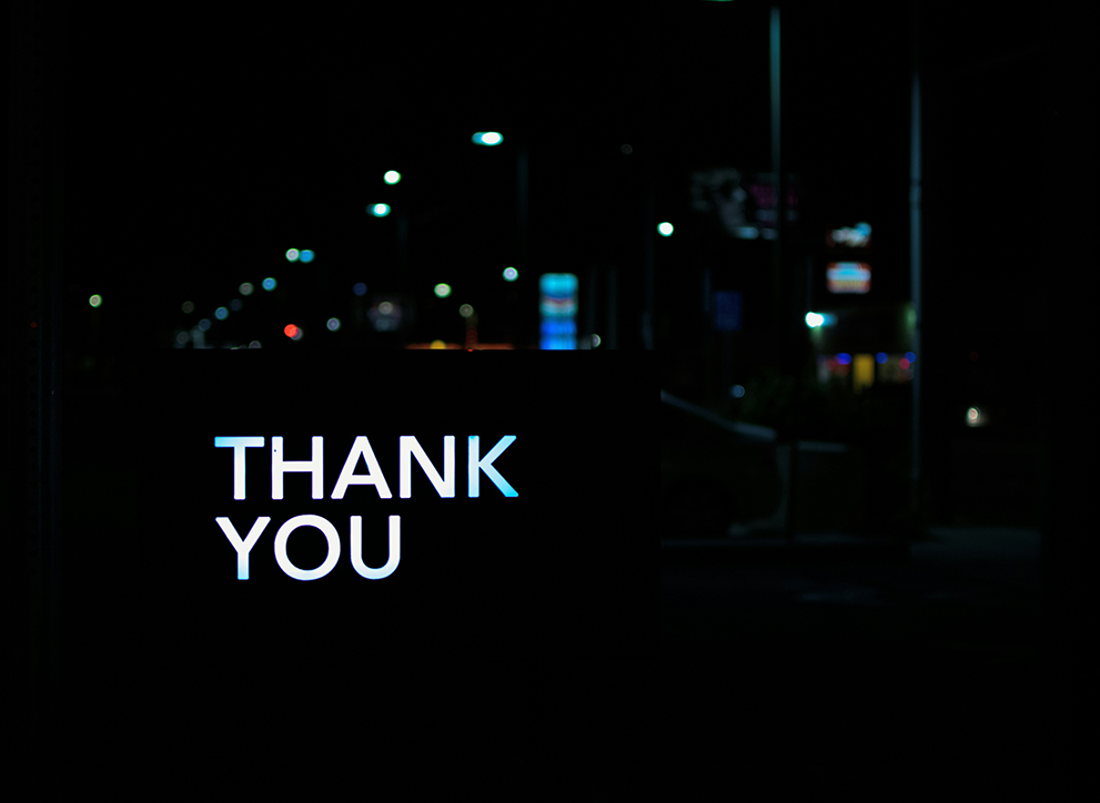 Photo of Thank You sign against a backdrop of a city at night.