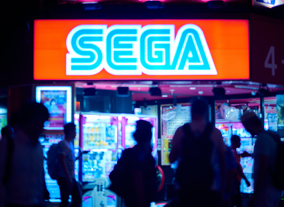 Photo shows people passing in front of Sega store in Japan, with Sega logo overhead. Photo by Jezael Melgoza on Unsplash.