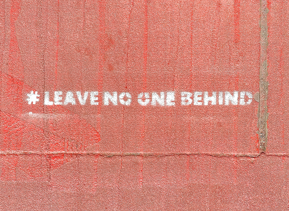 Wall stencilled with the phrase &#039;# Leave no one behind'.